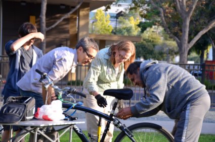 Bike Tent principal mechanic Bronwen Mauch (wearing glove) instructs a Bike Tent client and Bike Concord volunteers on a repair job.